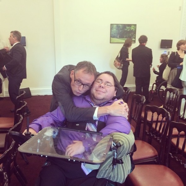 Dominick, at the White House, with his friend, Lawrence Carter Long, a disability rights activist. Dominick is wearing a purple button down and striped purple tie, and is in his power wheelchair. Lawrence is hugging him from behind, in his suit!